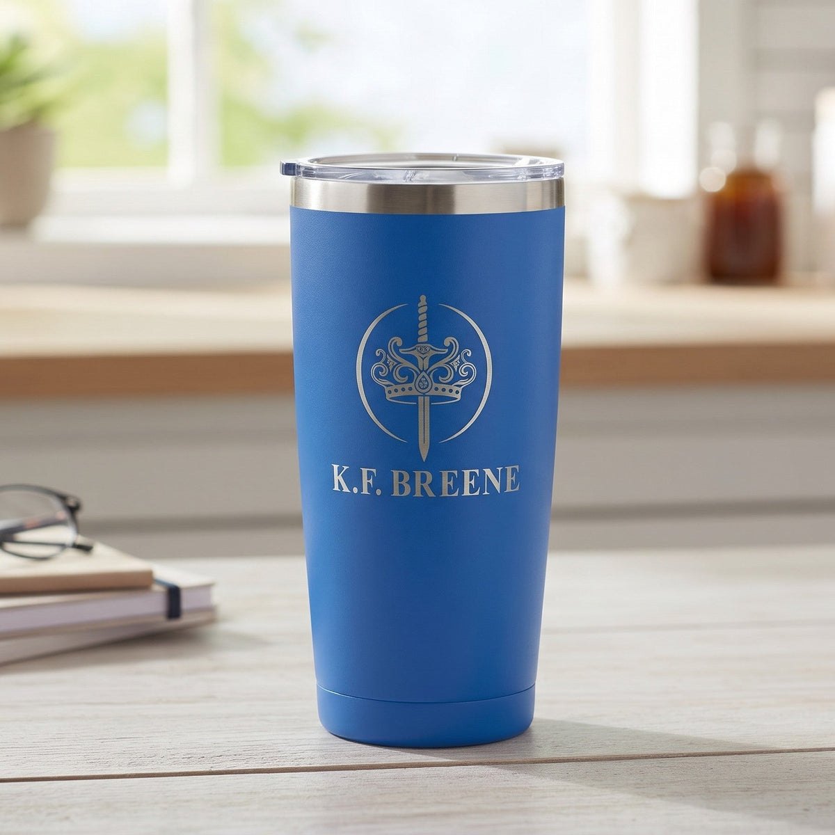 K.F. Breene Swag Shop blue insulated 20oz tall tumbler with etched sword and crown logo on a kitchen counter